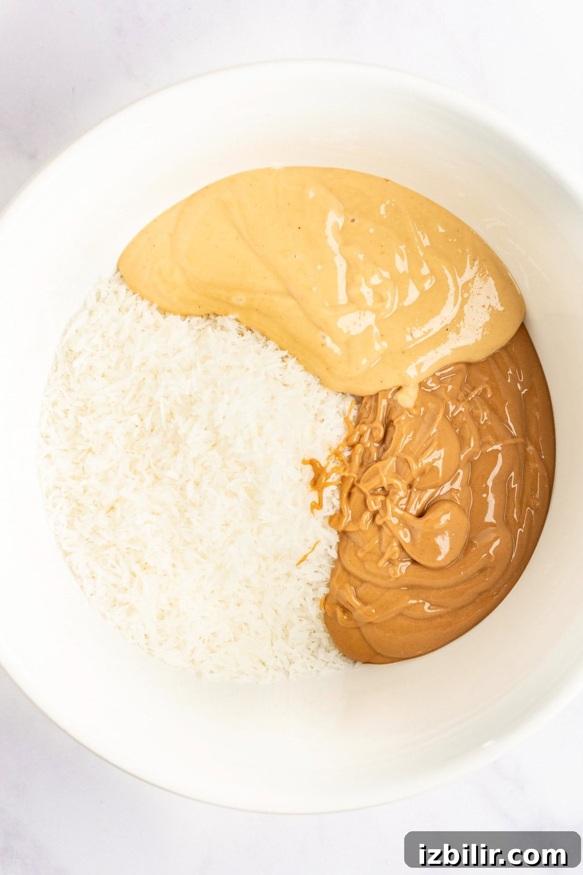 A bowl containing shredded coconut, smooth peanut butter, and crunchy peanut butter.