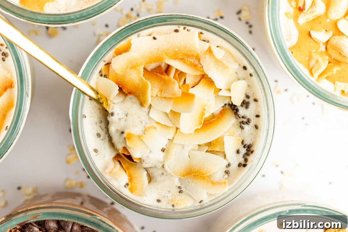 A glass bowl filled with a creamy mixture topped with toasted coconut flakes and chia seeds, with a gold spoon inserted into it. Other similar bowls are partially visible around it.