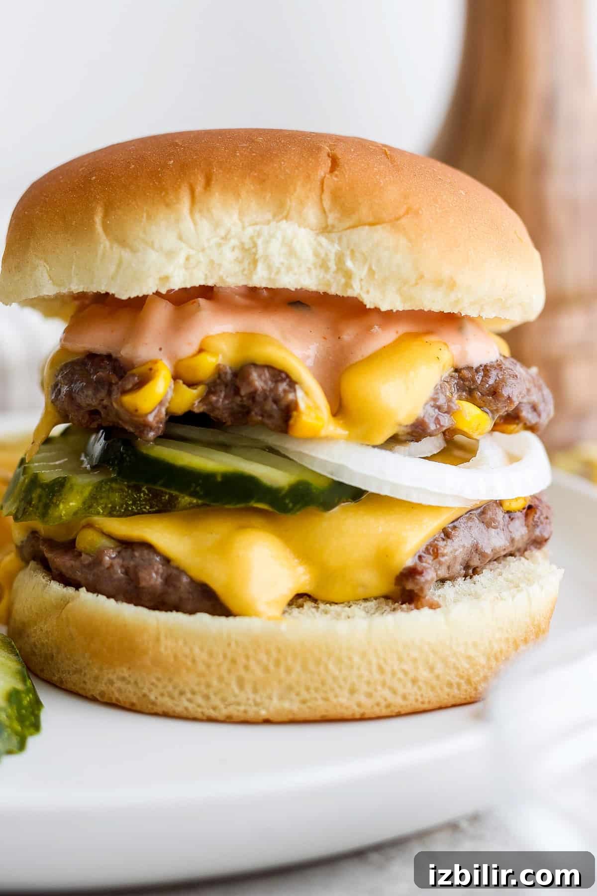 Loaded Sweet Corn Smash Burger Recipe 5 A double cheeseburger with pickles, onions, and sauce on a white plate.