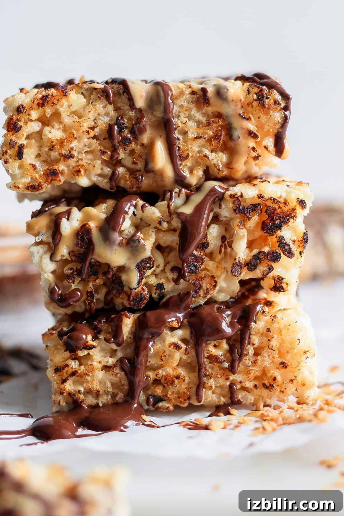 Toasted Marshmallow Rice Krispies Treats Recipe 2 Stack of three toasted rice Krispie treats drizzled with chocolate and peanut butter on a white surface.
