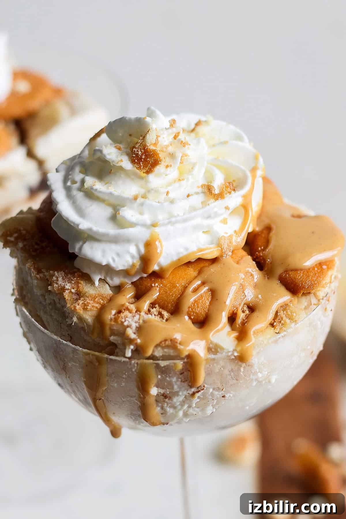 A dessert in a glass featuring layers of caramel, ice cream, whipped cream, and crumbled cookies on top, reminiscent of a peanut butter banana ice box cake.