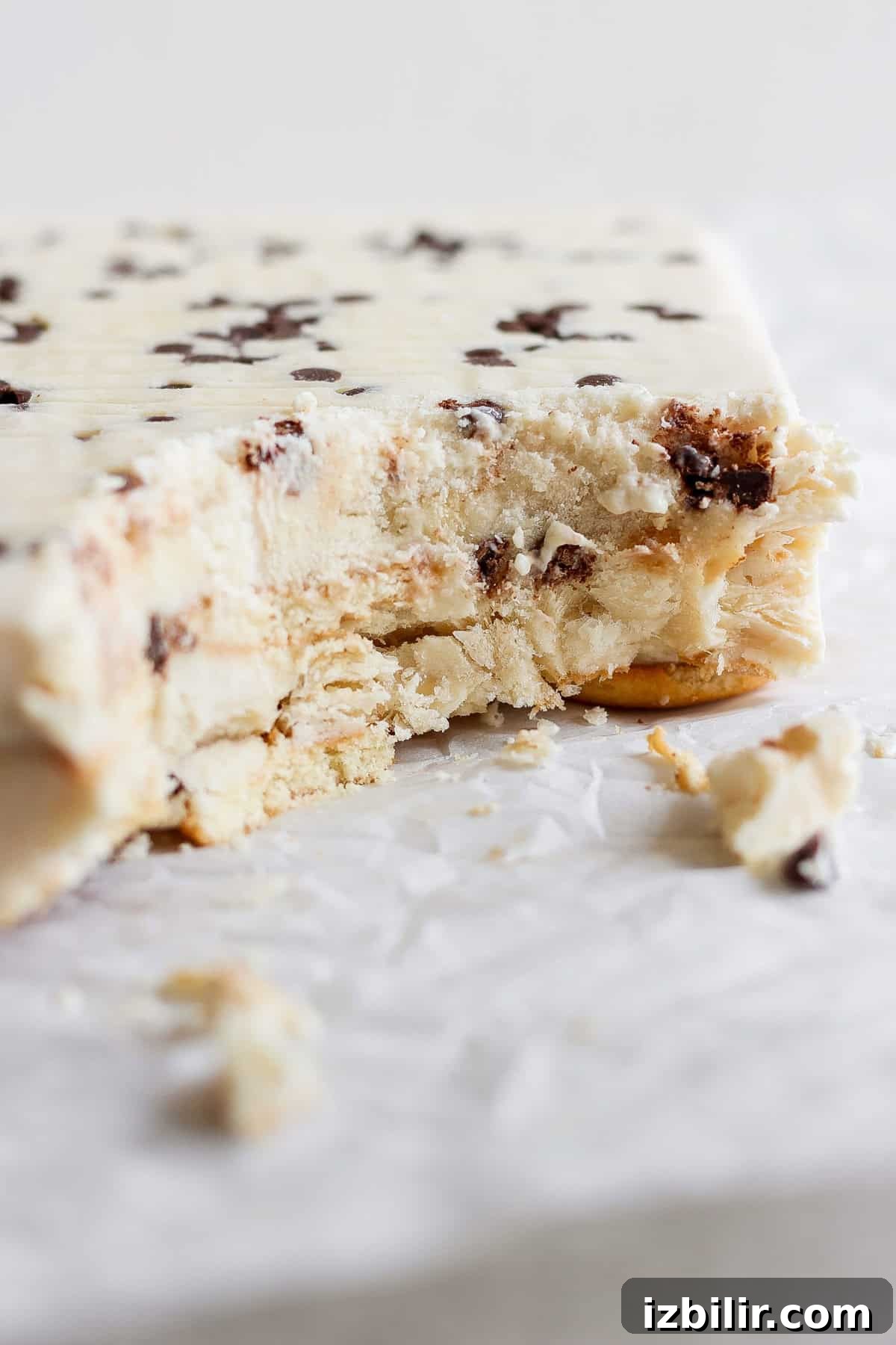 A partially eaten ice cream cake with chocolate chips and a hint of peanut butter banana lies on white parchment paper.
