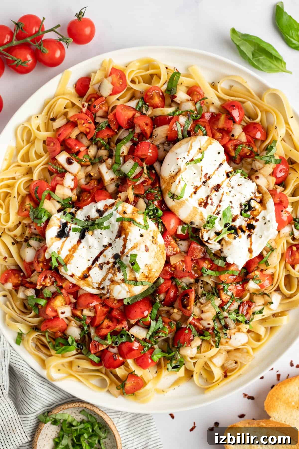 A plate of pasta topped with fresh chopped tomatoes, basil, two poached eggs, and a drizzle of balsamic glaze, garnished with black pepper.