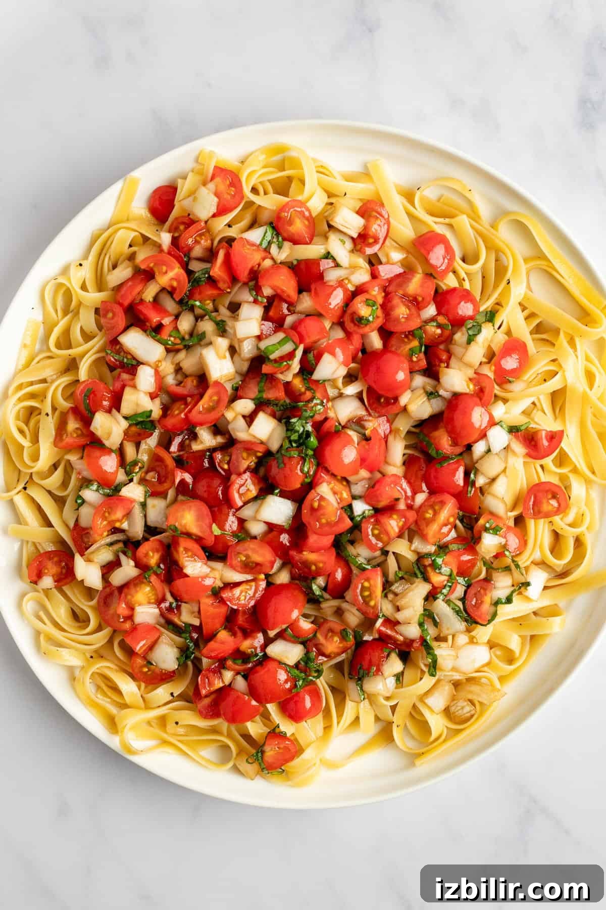 A plate of fettuccine pasta topped with chopped tomatoes, onions, and herbs.