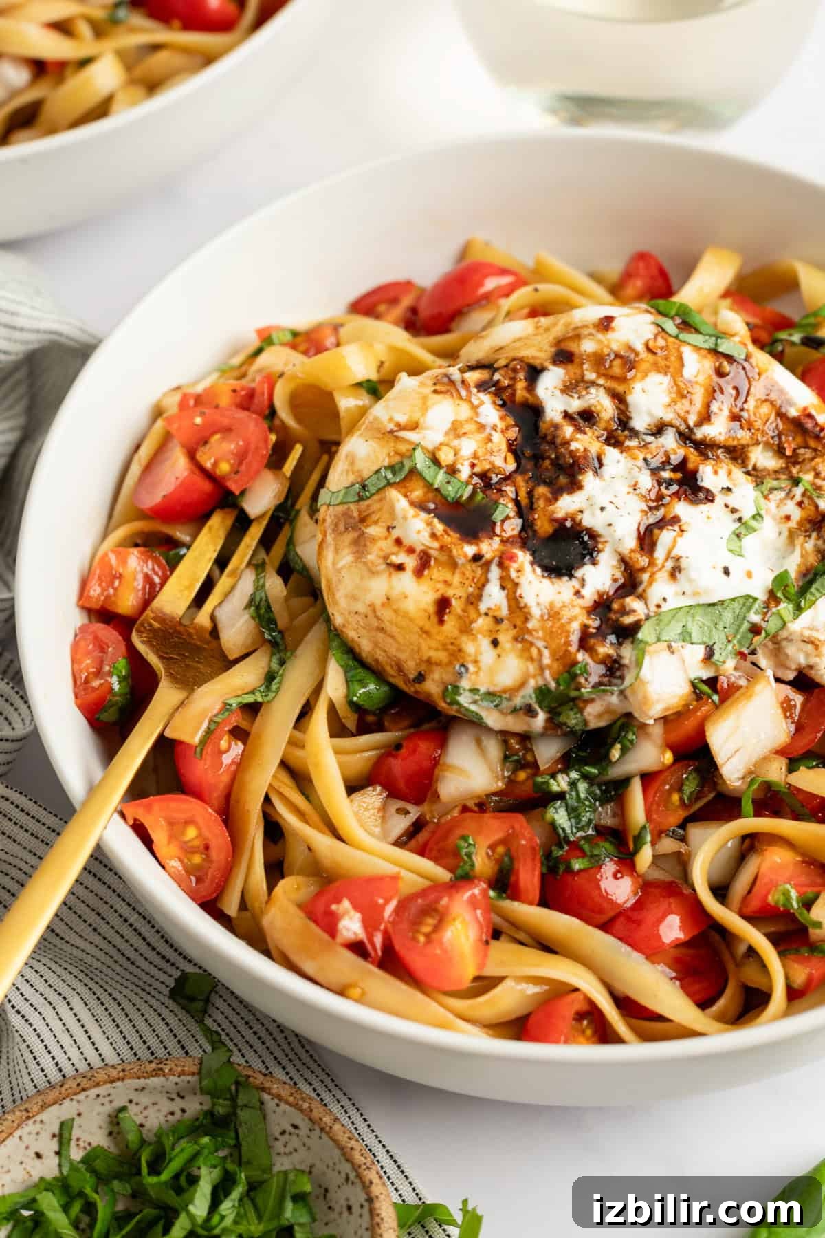 A bowl of fettuccine pasta topped with a grilled chicken breast, cherry tomatoes, and basil, drizzled with a creamy sauce.