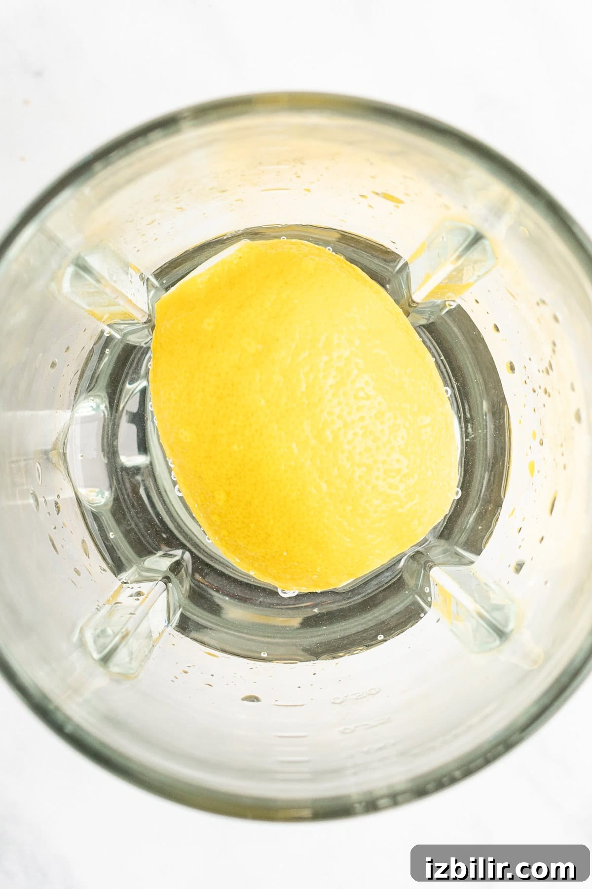 A halved lemon sits in a blender jar, viewed from above.
