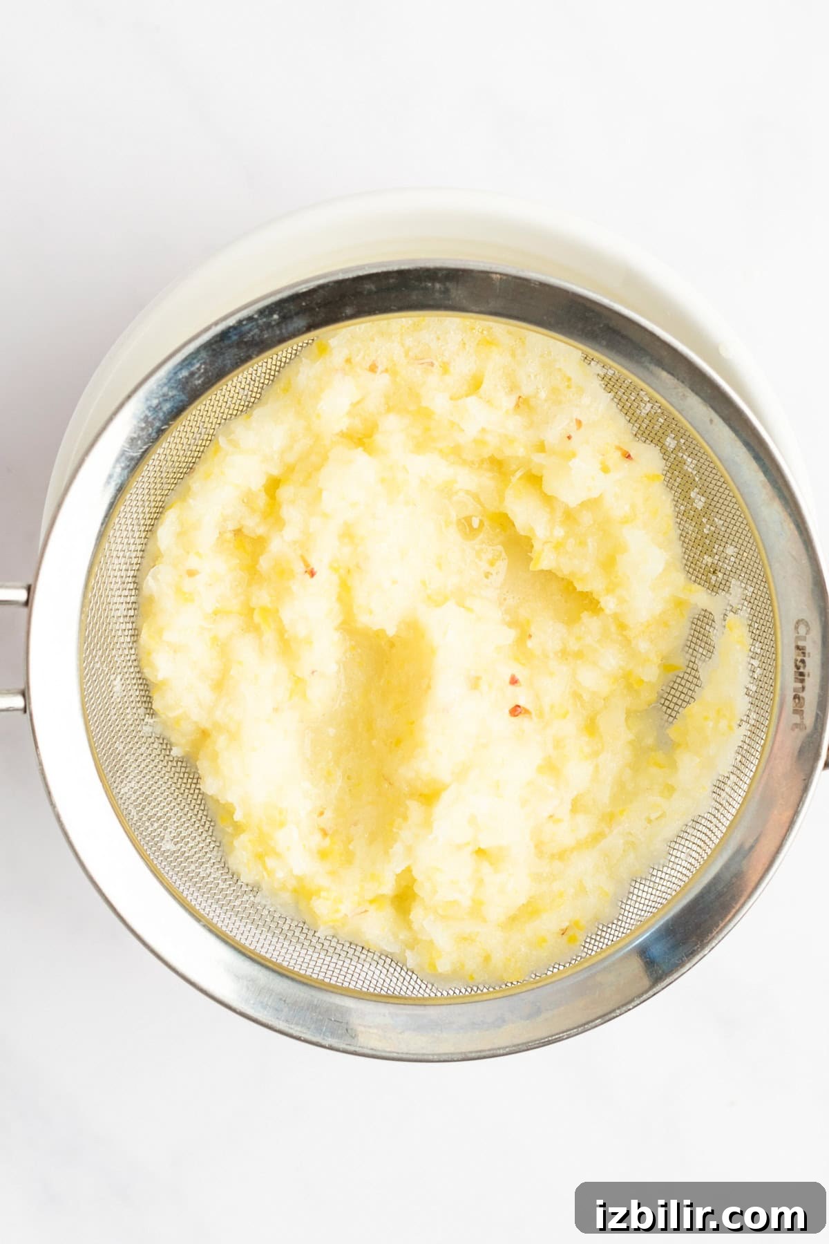 A metal sieve containing mashed potatoes over a white bowl.