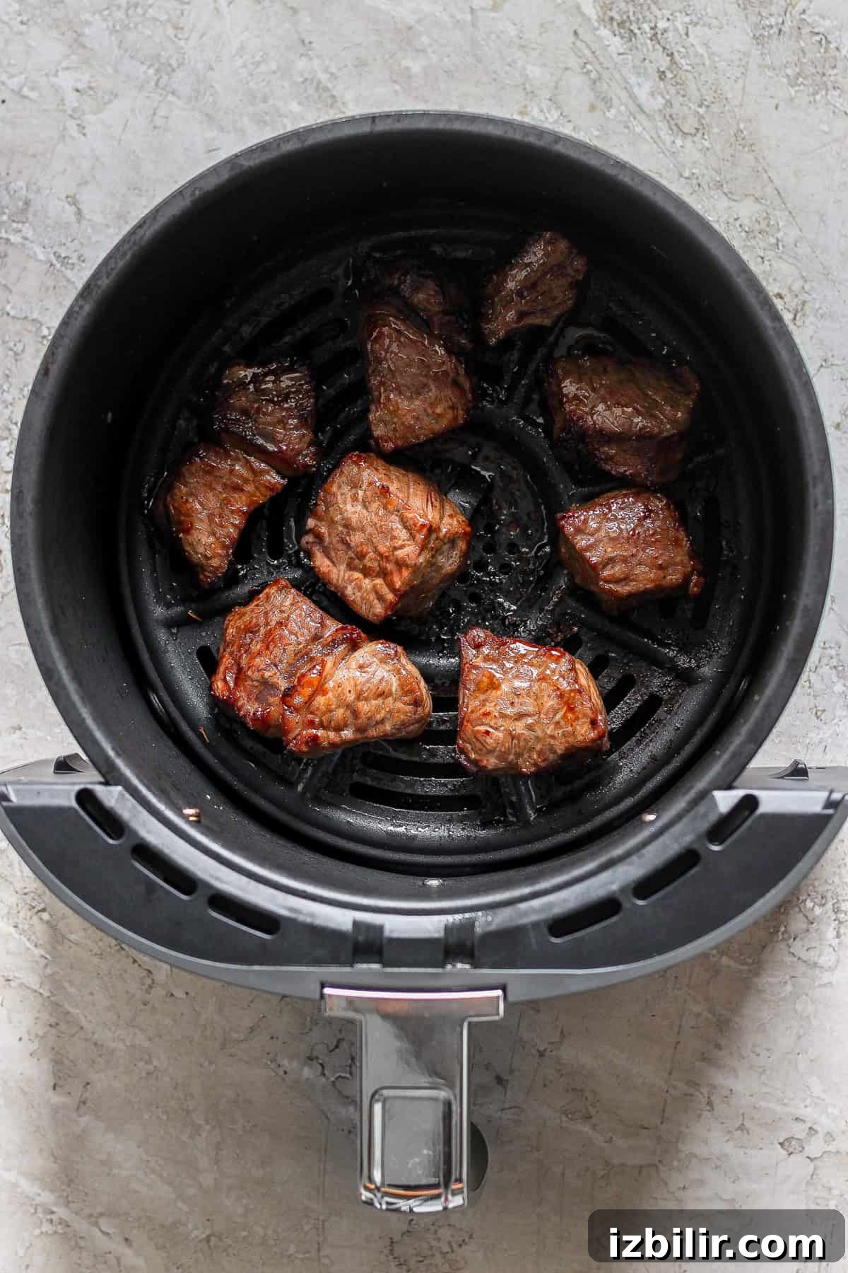 Crispy Air Fryer Steak Bites with Garlic Butter 6 Chunks of cooked meat resting in an air fryer basket.