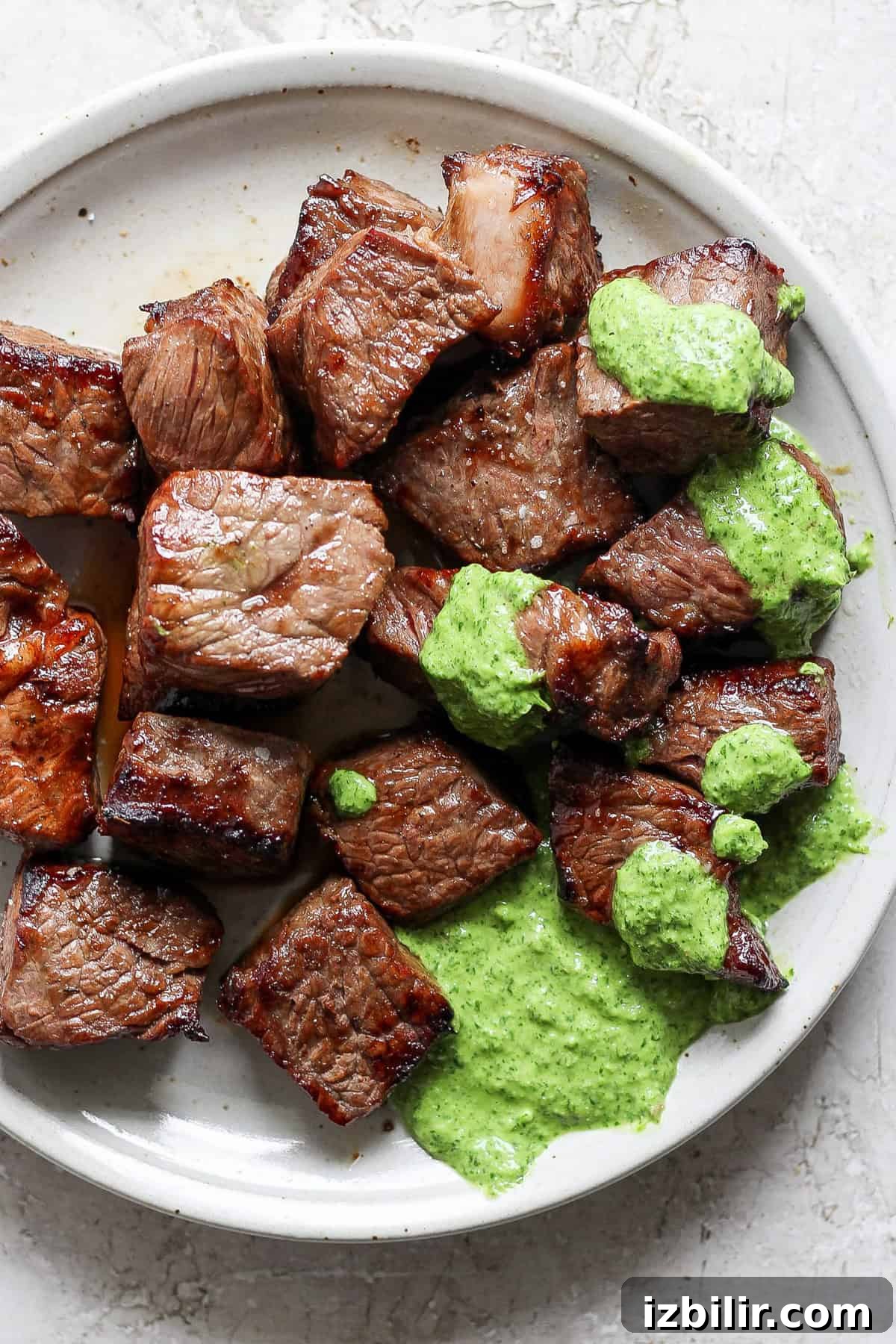 Crispy Air Fryer Steak Bites with Garlic Butter 5 A white plate with grilled steak bites topped with a green herb sauce.