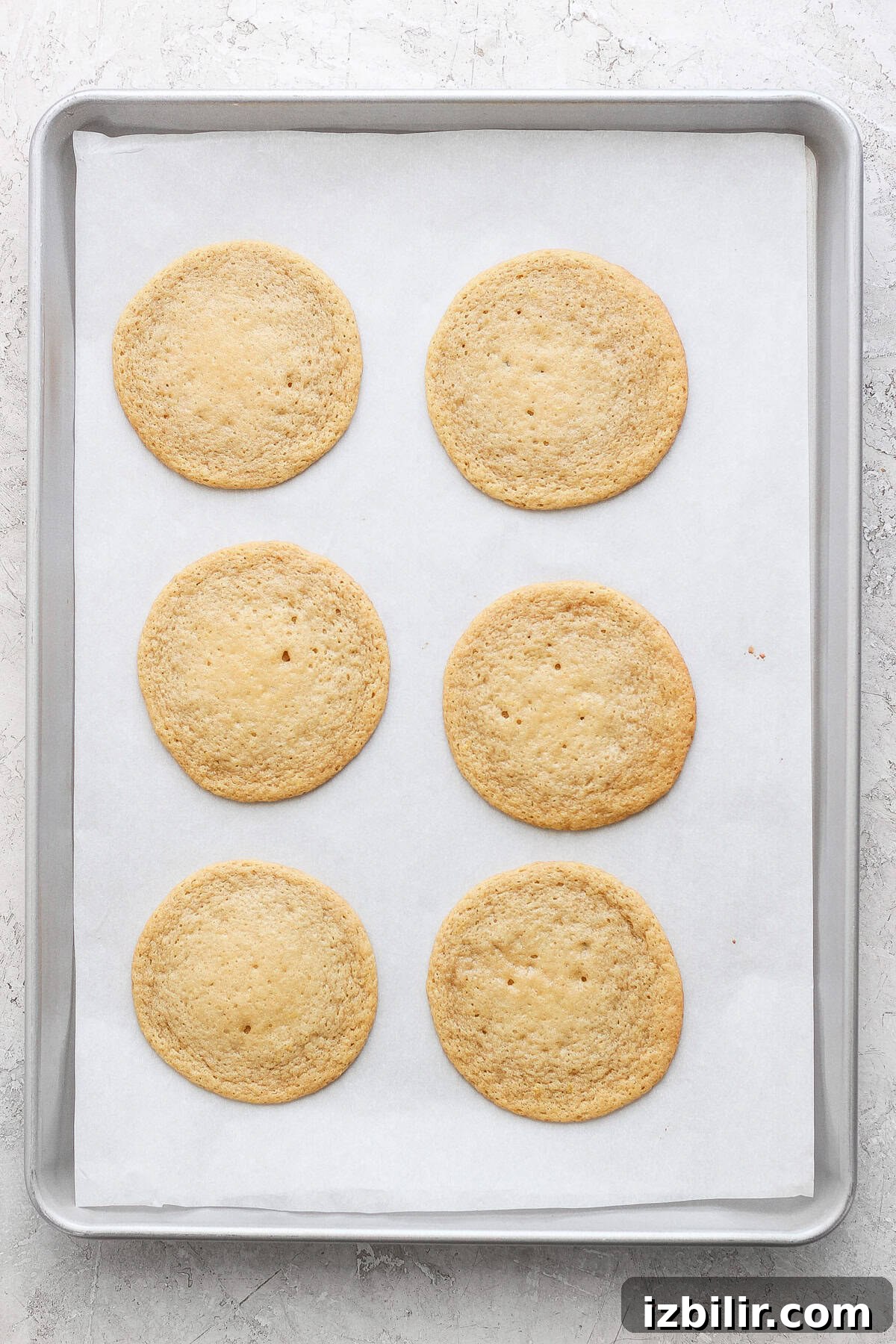 Zesty Lemon Cookies with Cream Cheese Frosting 3 Six round lemon cookies with cream cheese frosting rest on a parchment-lined baking sheet.