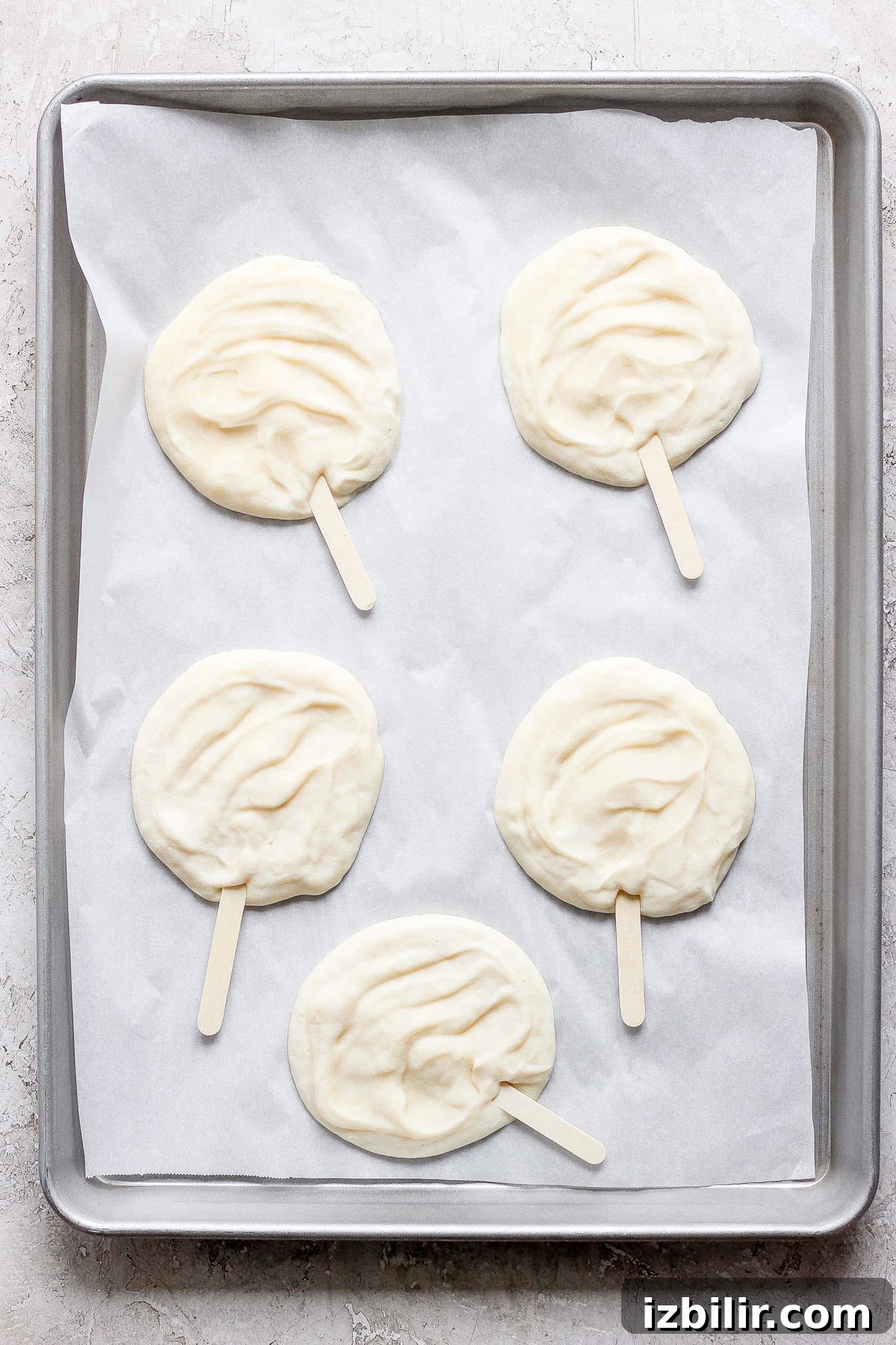Four raw popsicle-shaped dough pieces on parchment paper in a gray baking tray.