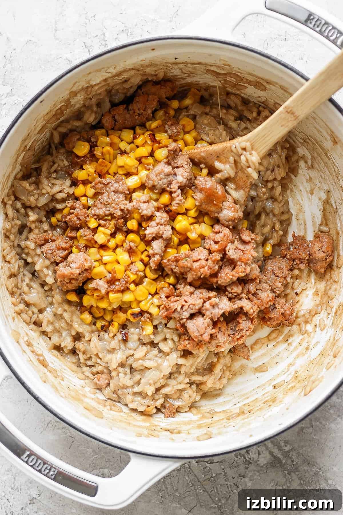 A pot of risotto with corn and ground sausage being stirred with a wooden spoon.
