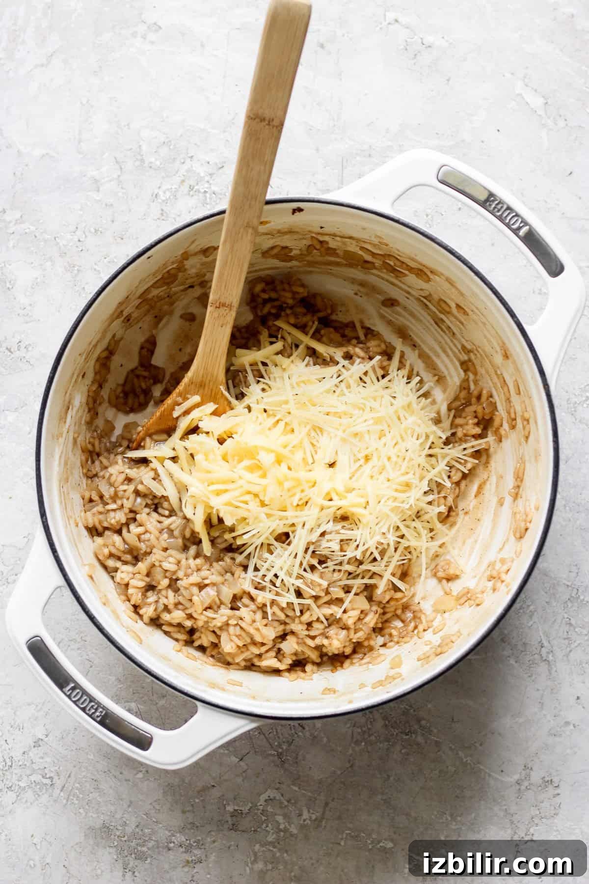 A wooden spoon rests in a white pot containing risotto, with grated cheese on top, ready to be stirred in.