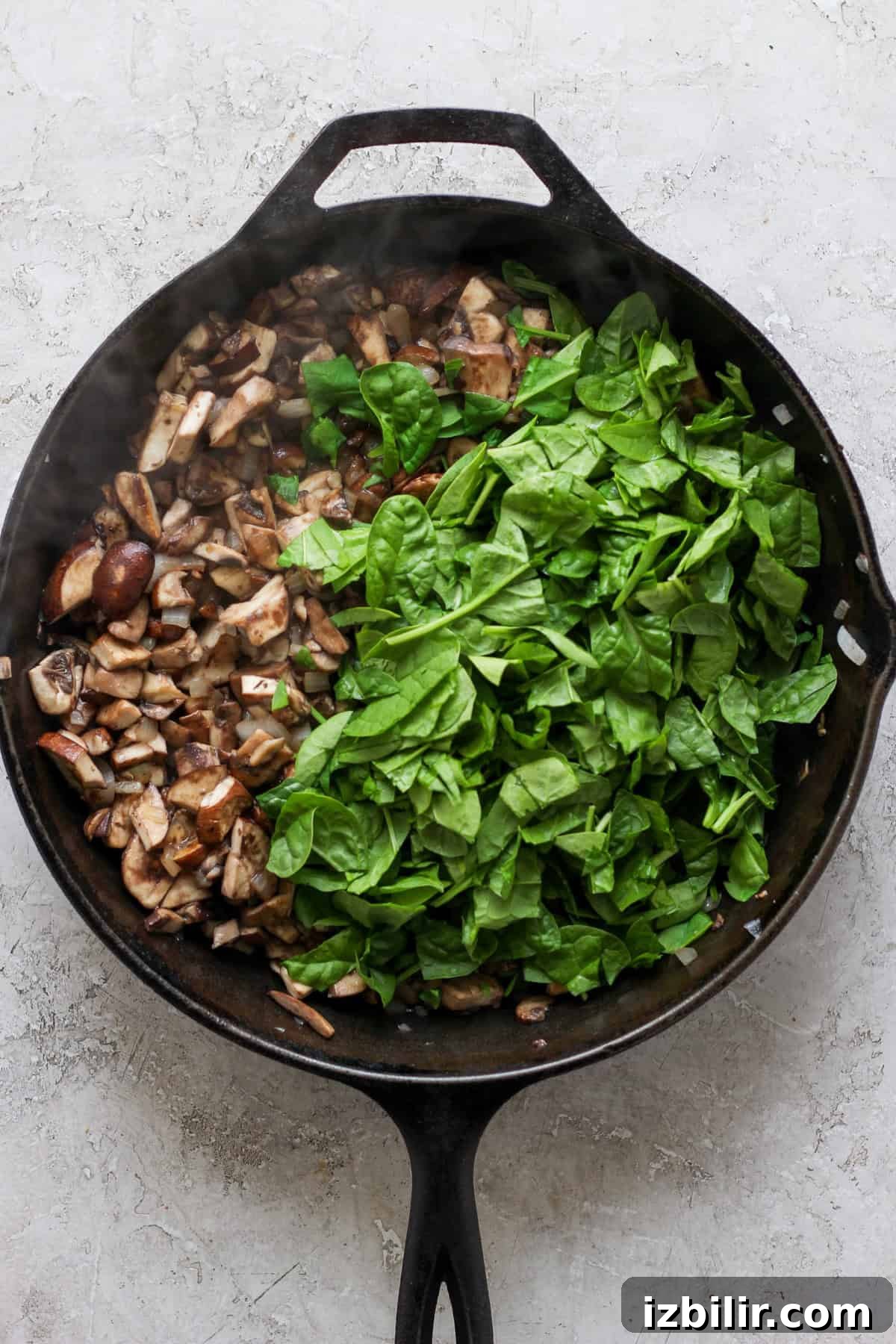 Pesto Lasagna Recipe with Fresh Basil and Mozzarella 3 A cast-iron skillet filled with chopped mushrooms on one side and fresh spinach on the other, set on a light-colored surface.