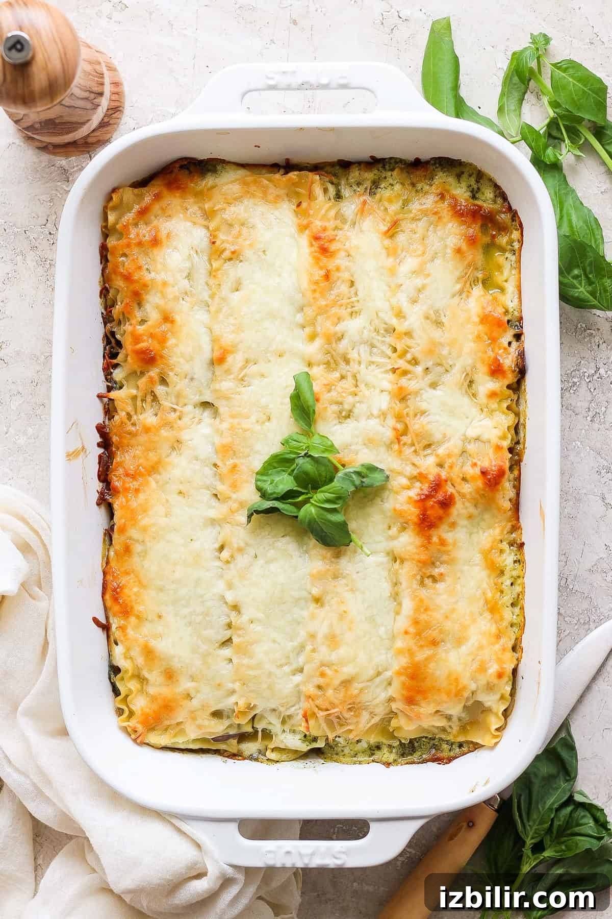 Pesto Lasagna Recipe with Fresh Basil and Mozzarella 5 A baked lasagna in a white rectangular dish, topped with melted cheese and garnished with fresh basil leaves.