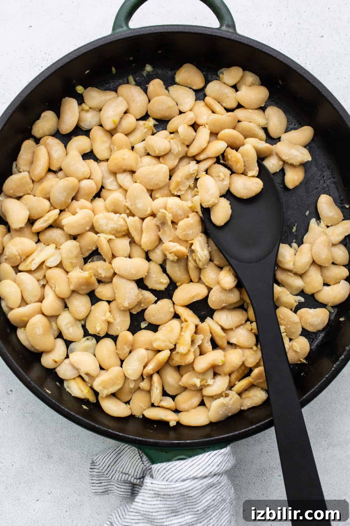 Classic British Beans on Toast Recipe 4 White beans in a frying pan with a black spatula.