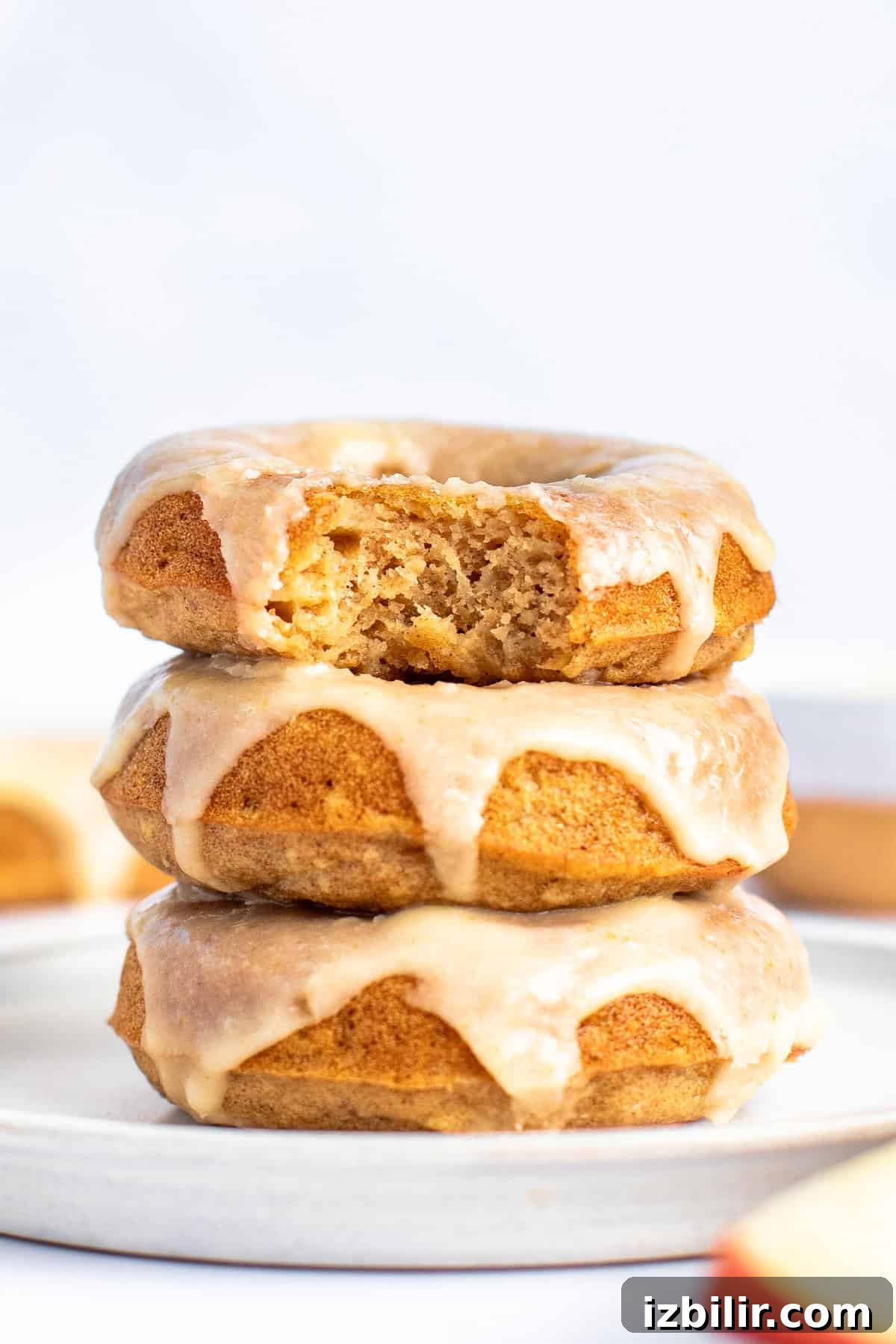 Apple Cider Donuts Recipe with Cinnamon Sugar 2 A stack of three glazed donuts on a white plate, with the top donut partially eaten, showing a golden brown interior.
