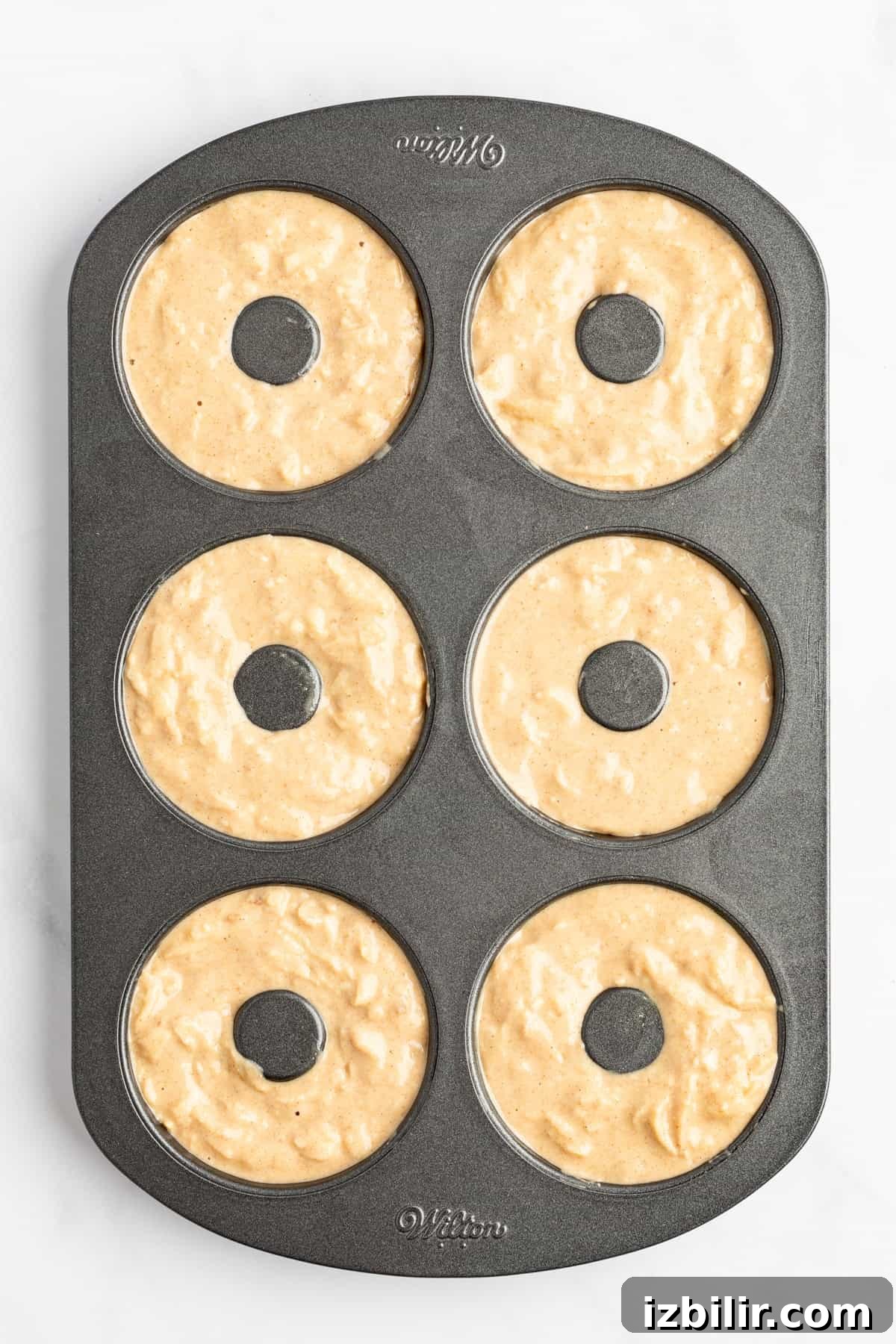 Apple Cider Donuts Recipe with Cinnamon Sugar 5 A six-cavity donut baking pan filled with unbaked donut batter, ready to be placed in the oven.