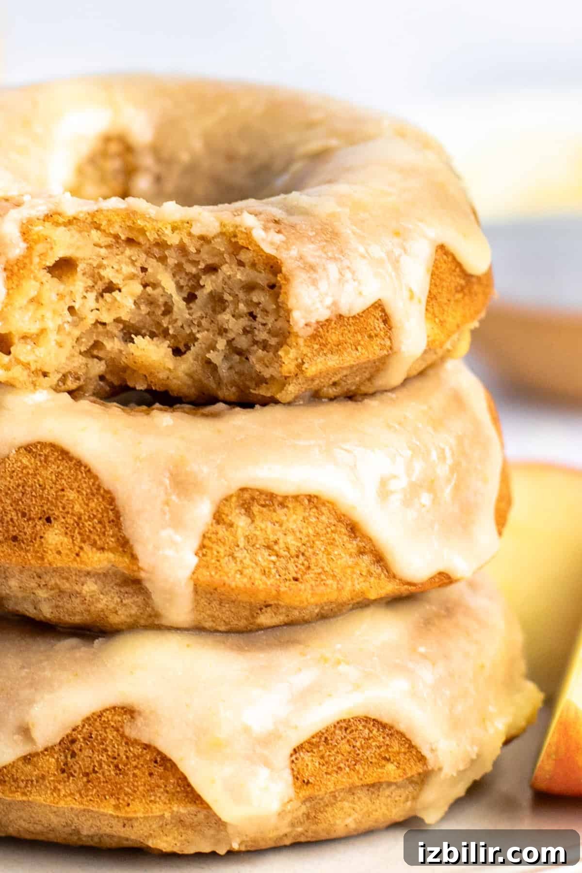 Apple Cider Donuts Recipe with Cinnamon Sugar 8 A stack of three glazed donuts with a bite taken out of the top one, showing their soft interiors.