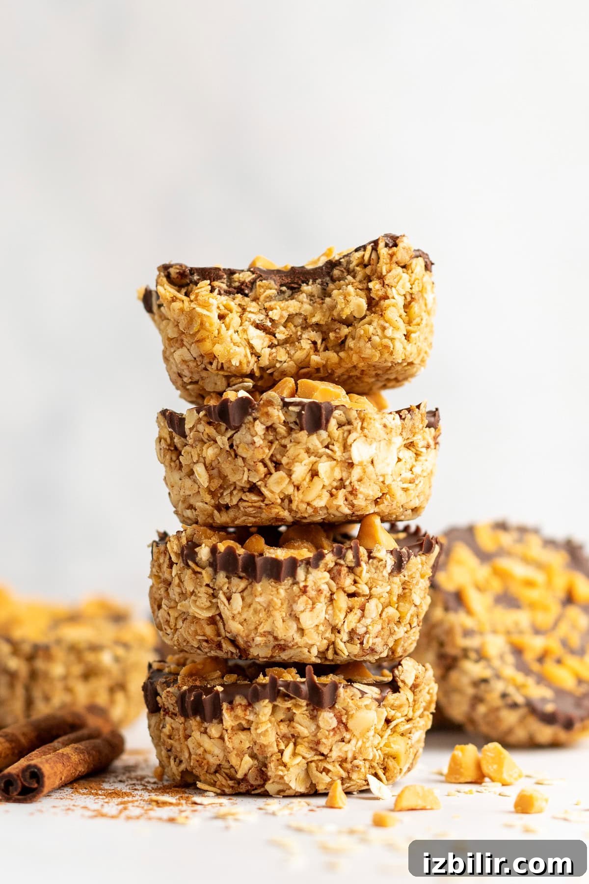 Pumpkin Spice Oatmeal Cups Recipe 2 A stack of four oat and chocolate chip granola cups with a bite taken out of the top one, sitting on a light surface with scattered ingredients around.