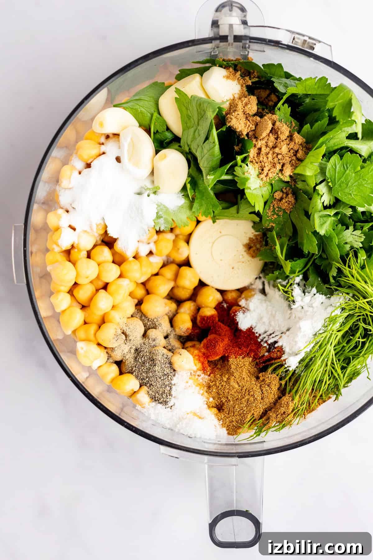 Crispy Homemade Falafel Recipe with Tahini Sauce 5 Food processor bowl filled with chickpeas, garlic, herbs, spices, and other falafel ingredients, viewed from above.