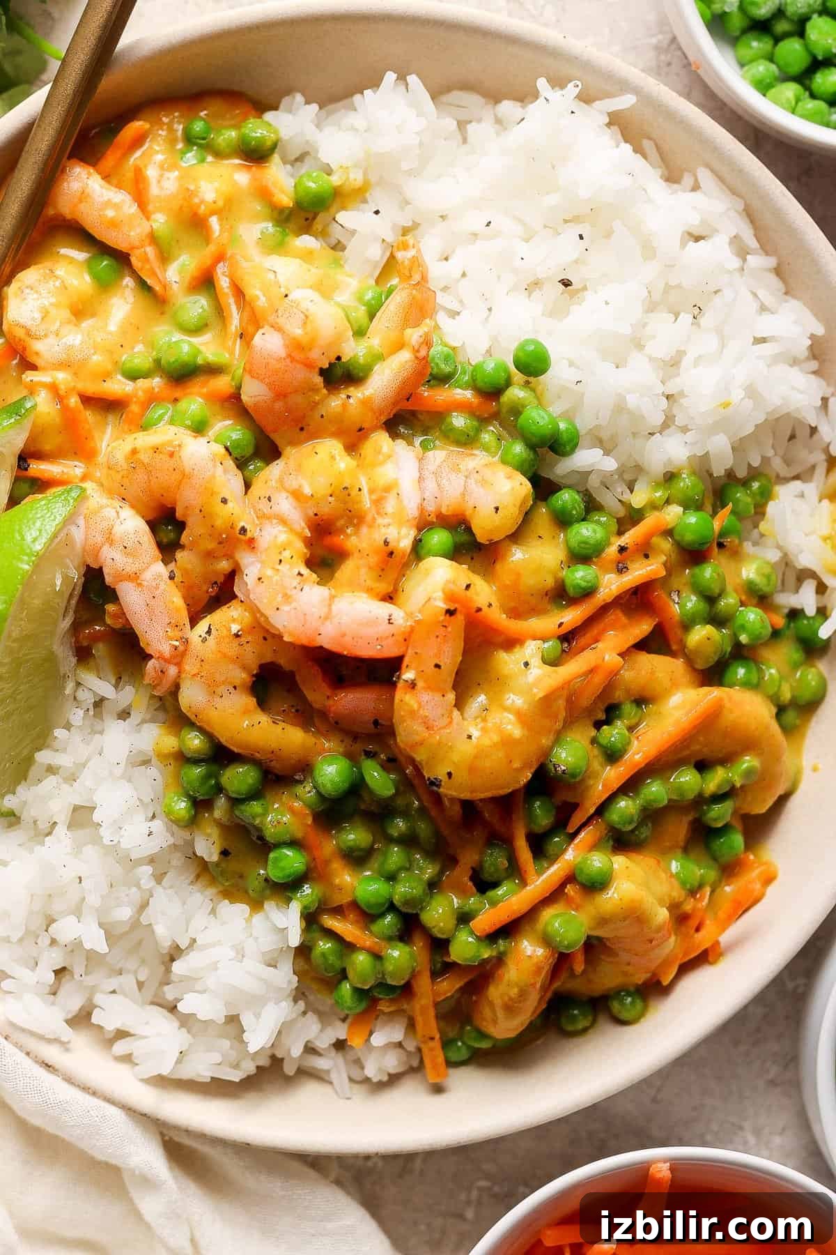 One-Pot Trader Joe's Yellow Curry Recipe 6 A bowl of white rice topped with shrimp and green peas in a creamy sauce, garnished with a lime wedge.
