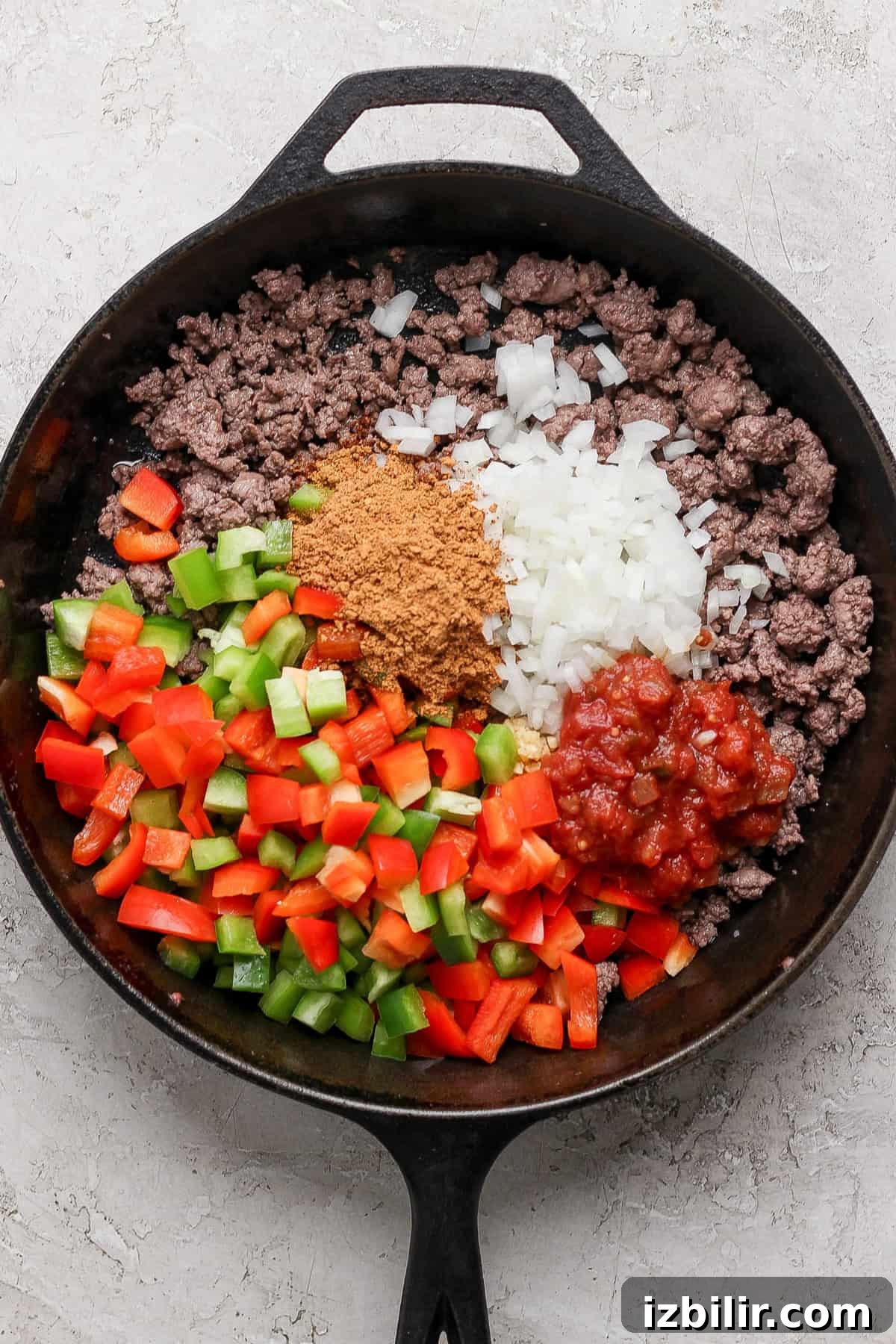 A cast iron skillet with cooked ground beef, peppers, onions, and salsa ready for layering in the lasagna.