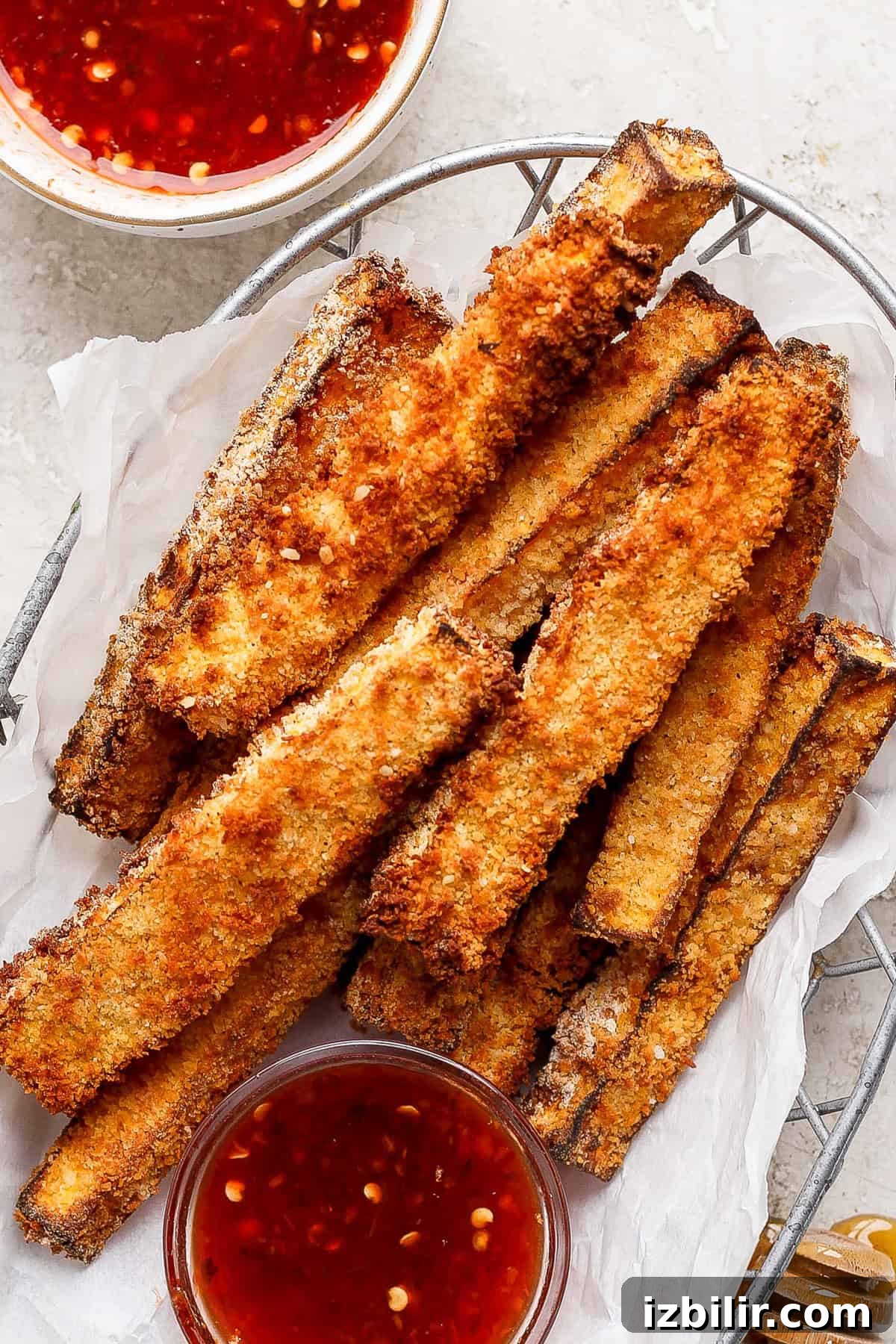 Air Fryer Butternut Squash Fries with Hot Honey Recipe 5 A basket filled with crispy, golden-brown breaded zucchini fries, accompanied by two small bowls of red dipping sauce.