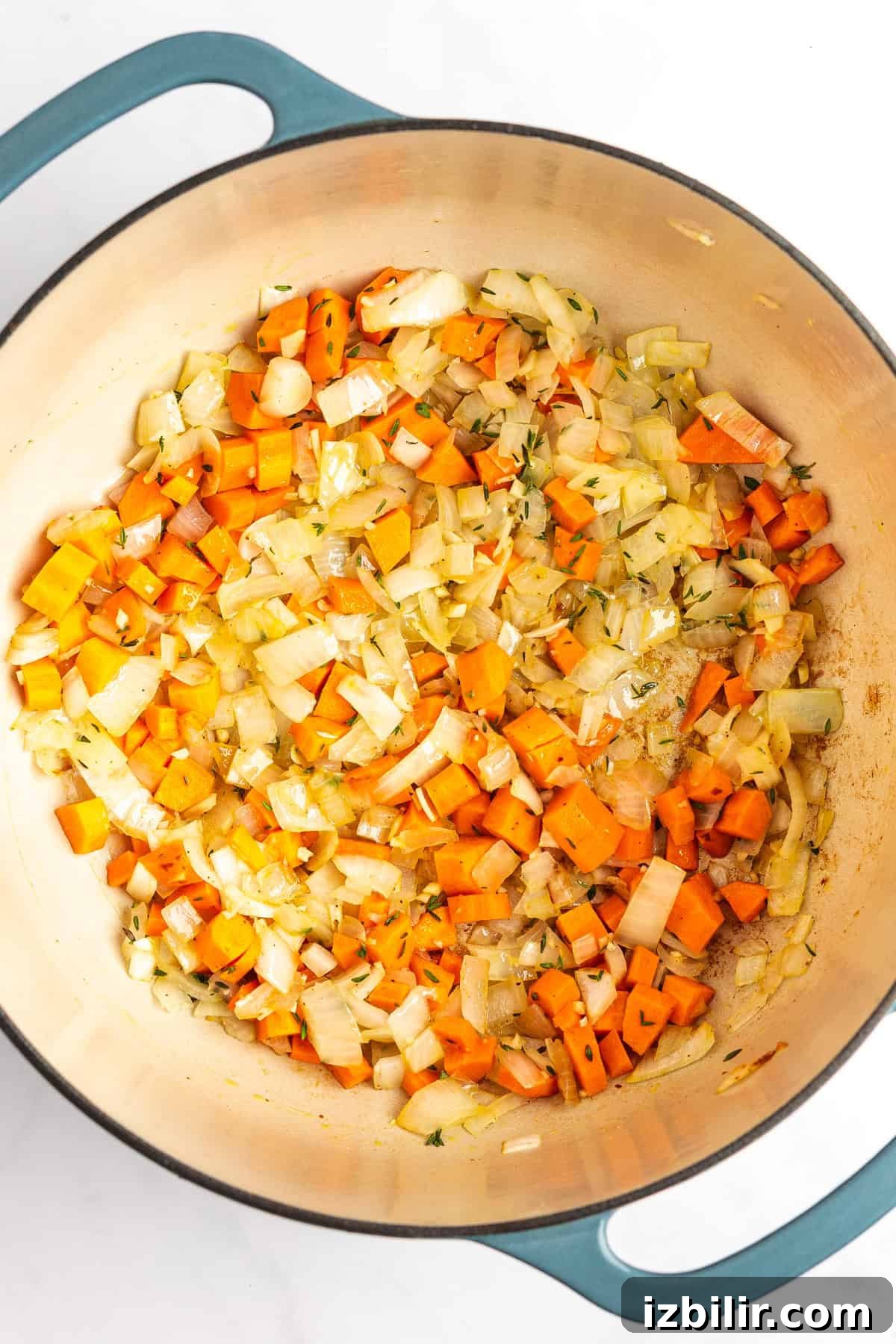 A pot containing sautéed diced onions and carrots.