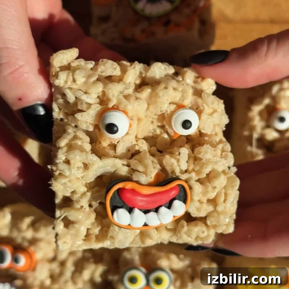 Brown Butter Chai Rice Krispie Treats Recipe 4 A Rice Krispies treat decorated with candy eyes and a mouth, resembling a goofy face, is held between two hands with black-painted nails.