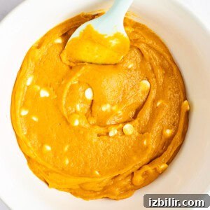 Chewy Pumpkin Blondies Recipe with Spiced Brown Sugar 9 A bowl containing orange cake batter with white chocolate chips mixed in and a light blue plastic spatula.