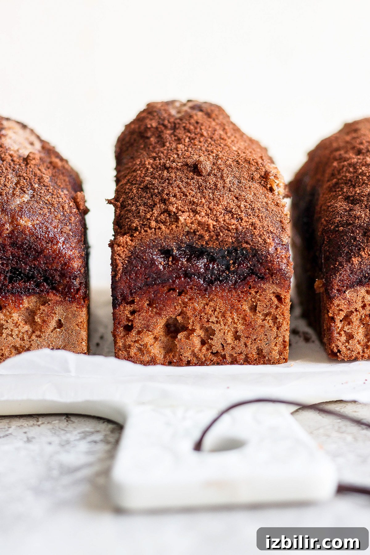 Mini Cinnamon Crunch Loaves Recipe 4 Close-up of three slices of marble cake arranged on a white cutting board. The cake has a distinct swirl pattern and a crumbly, textured top.