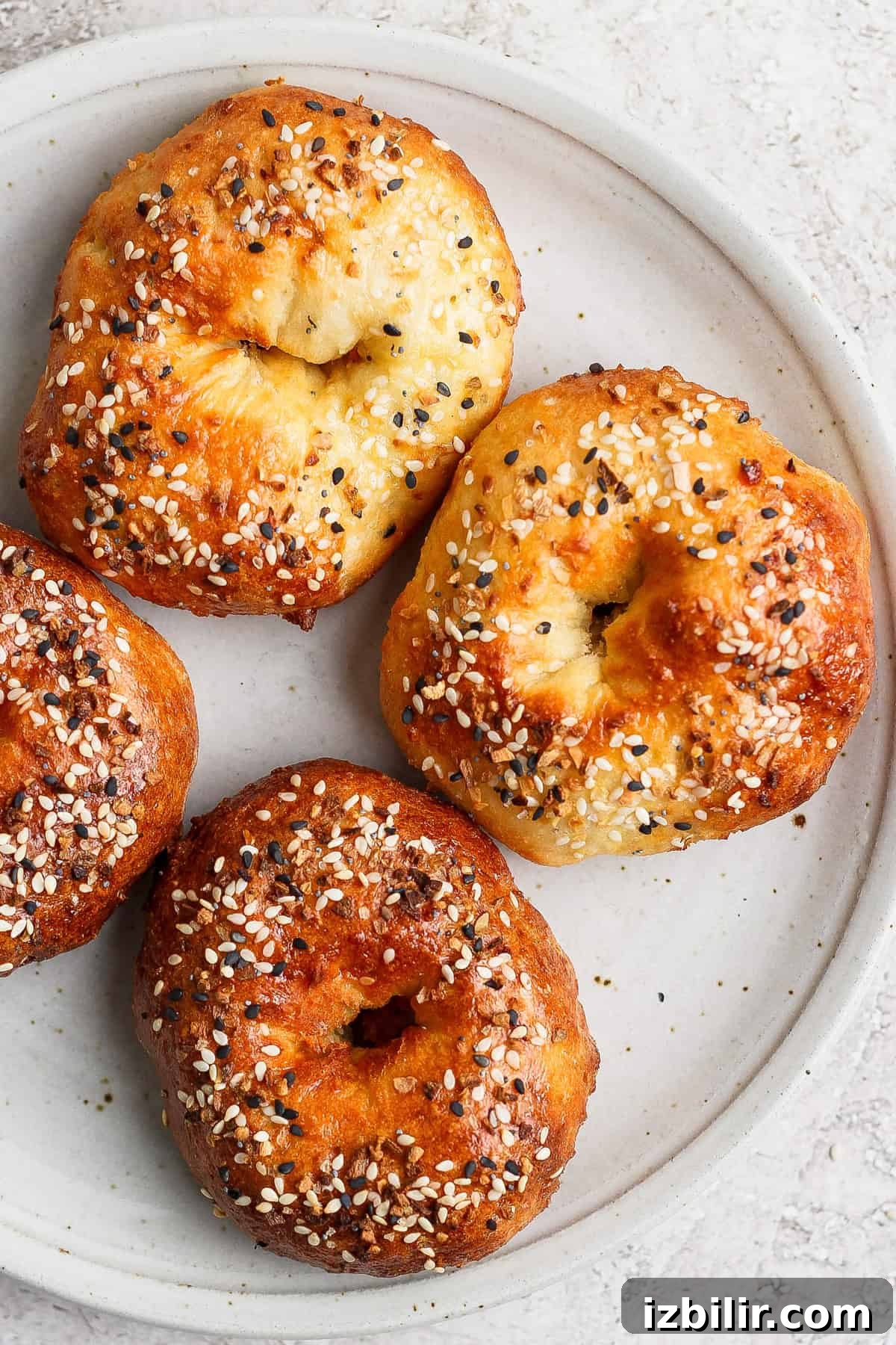 A white plate with four baked bagels topped with sesame seeds and seasonings.
