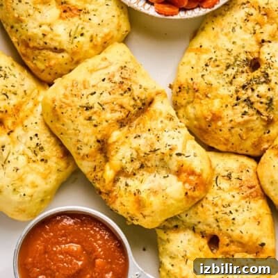Golden-brown stuffed bread rolls, reminiscent of delightful pizza hot pockets, are sprinkled with herbs and paired with a small bowl of tomato sauce.