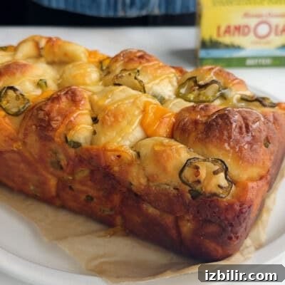 A loaf of pull-apart bread with melted cheese and sliced jalapeños on parchment paper.