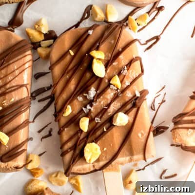 Chocolate-coated ice cream bar sprinkled with nuts and drizzled chocolate on parchment paper.
