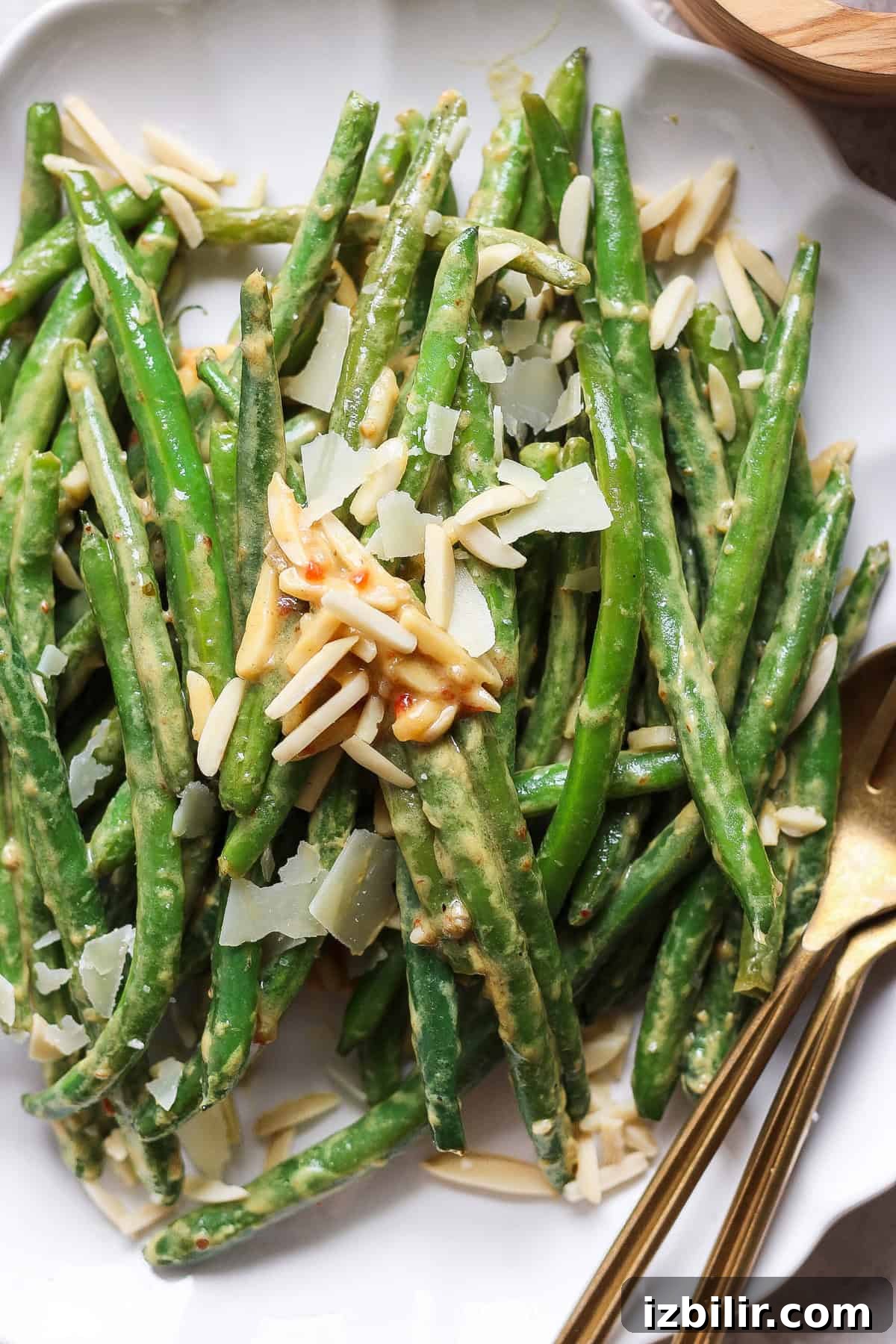 Grandma Ginny's Green Bean Sauté Recipe 7 A plate of green beans topped with shaved Parmesan cheese and almond slivers, with serving utensils on the side.
