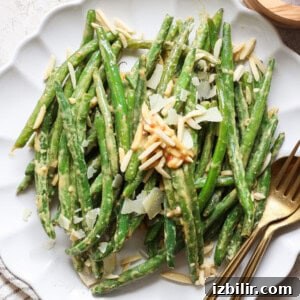 Grandma Ginny's Green Bean Sauté Recipe 8 A plate of green beans topped with shaved almonds and cheese, accompanied by a fork and knife.