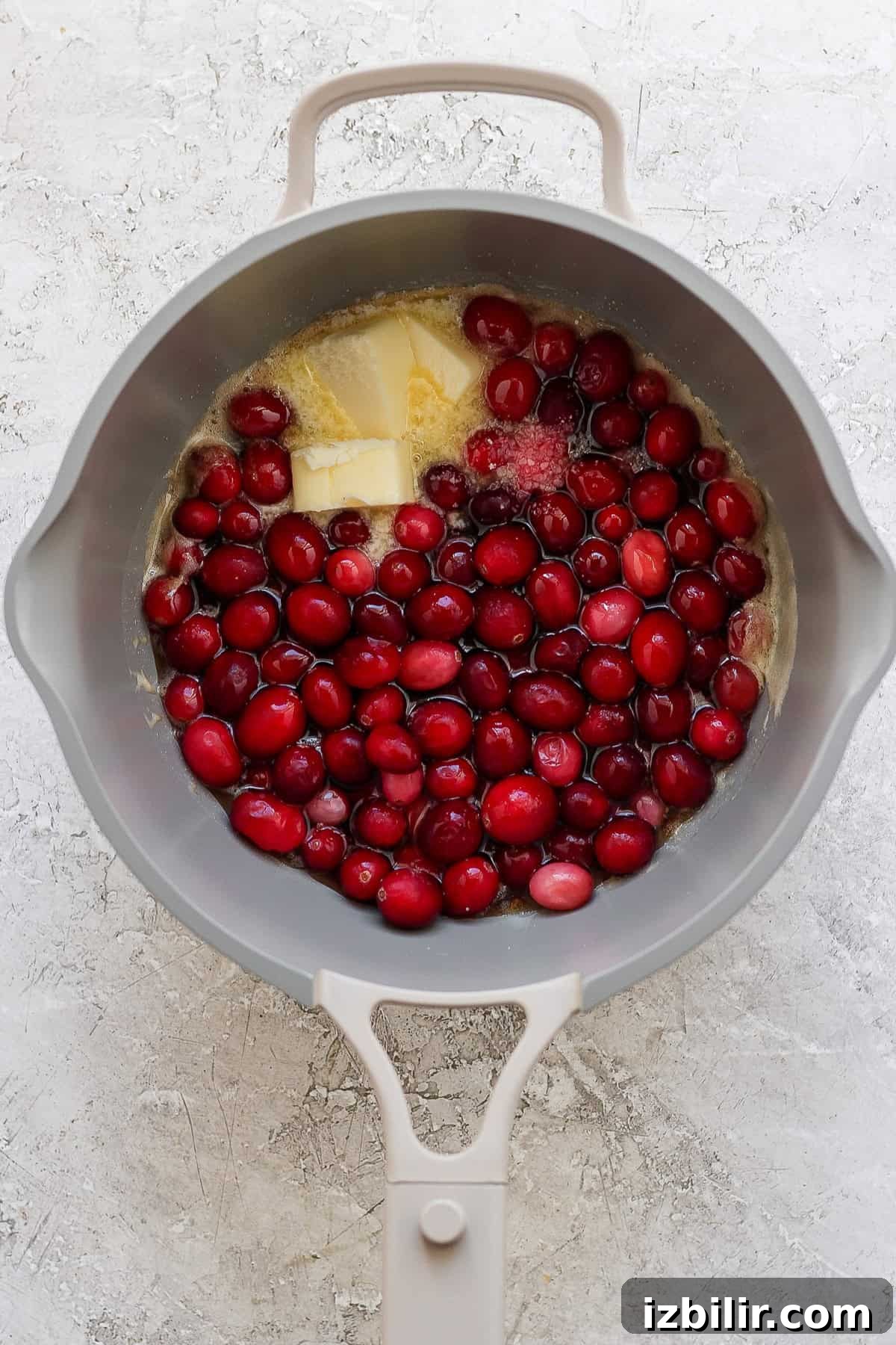 Grandpa Dick's Maple Cranberry Sweet Potatoes Recipe 5 A gray pot contains raw cranberries, a block of butter, and sugar on a light textured surface.