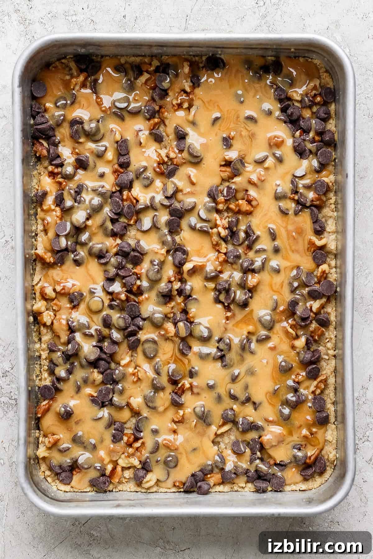 A baking tray filled with a dessert topped with melted caramel, chocolate chips, and chopped nuts.