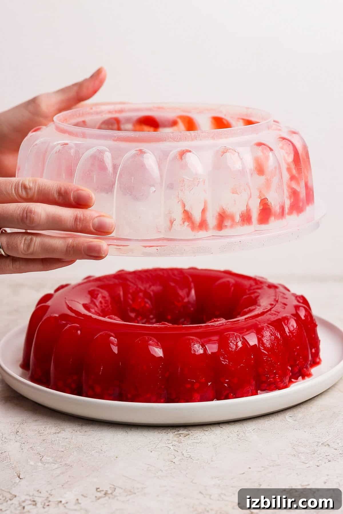 Nanie Arlene's Vintage Jello Mold Recipe 4 Hands removing a mold from a red gelatin dessert on a white plate.