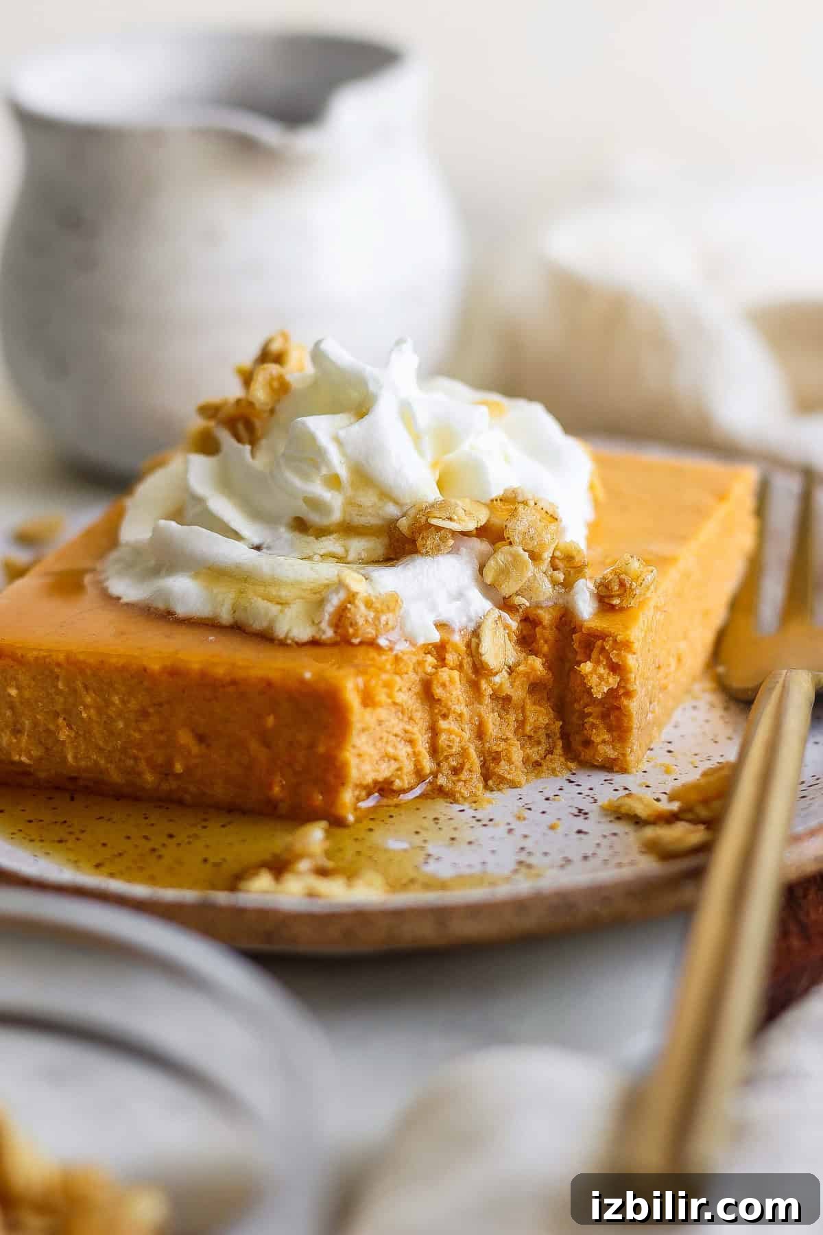 A slice of pumpkin cheesecake topped with whipped cream, granola, and drizzled with syrup, on a plate with a fork.