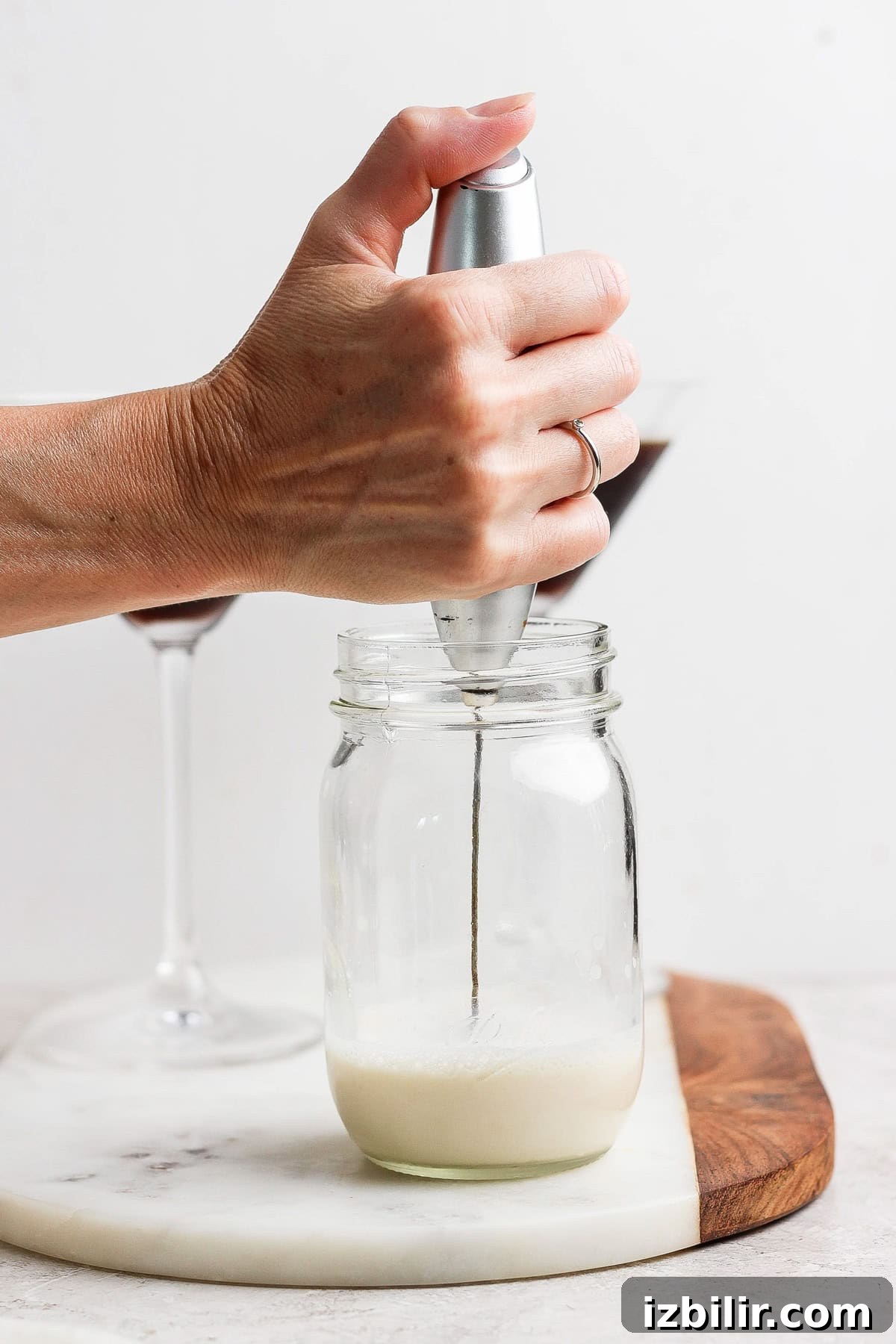 Brown Sugar Shaken Espresso Martini Recipe 3 A hand holds a milk frother in a glass jar creating foam