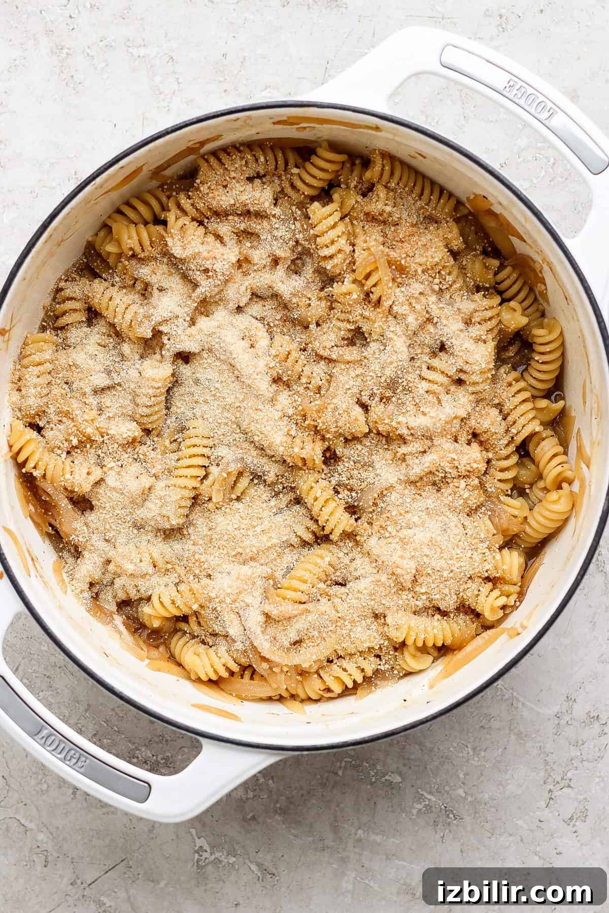 A pot of rotini pasta topped with a layer of grated cheese and breadcrumbs.