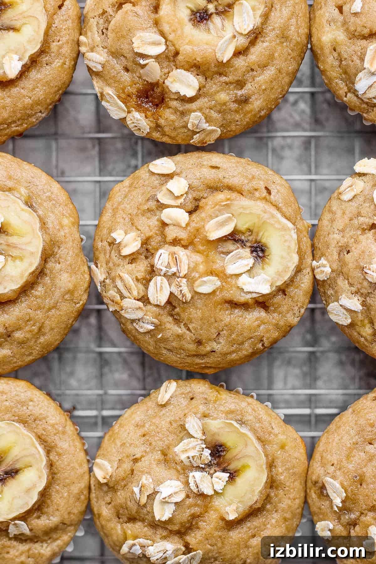 Banana oat muffins on a cooling rack, topped with banana slices and oats.