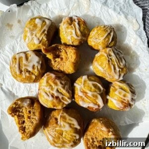 Crispy Air Fryer Pumpkin Bagel Bites Recipe 4 A dozen small, round cakes with white icing drizzle, some with bites taken out, arranged on crumpled parchment paper.