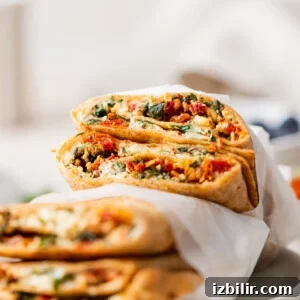 A wrap cut in half, filled with vegetables and cheese, stacked on a parchment paper-lined surface.