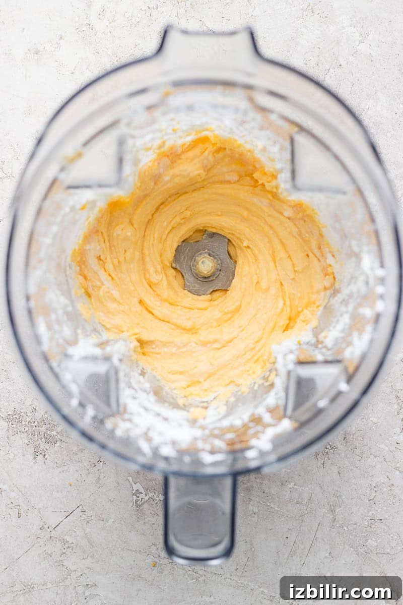 Creamy Whipped Cottage Cheese Macaroni and Cheese 3 Top view of a blender with creamy, whipped mixture inside, surrounded by a dusting of white powder on the container's edges.