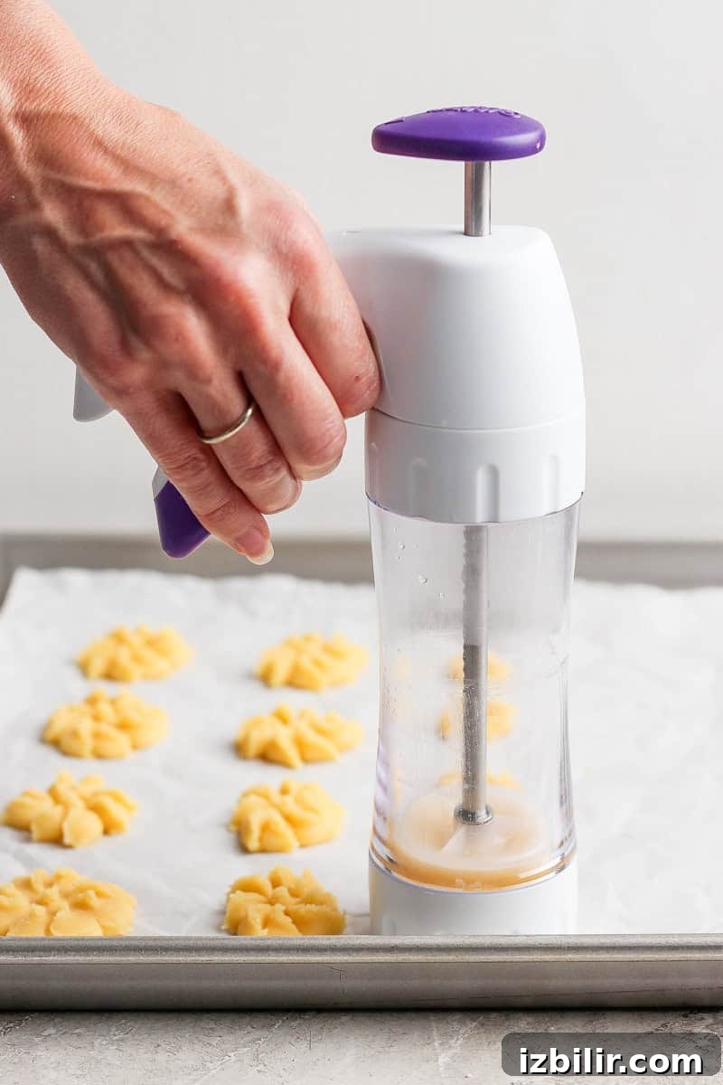 A hand pressing cookie dough onto a baking sheet using a cookie press, forming flower-shaped cookies.