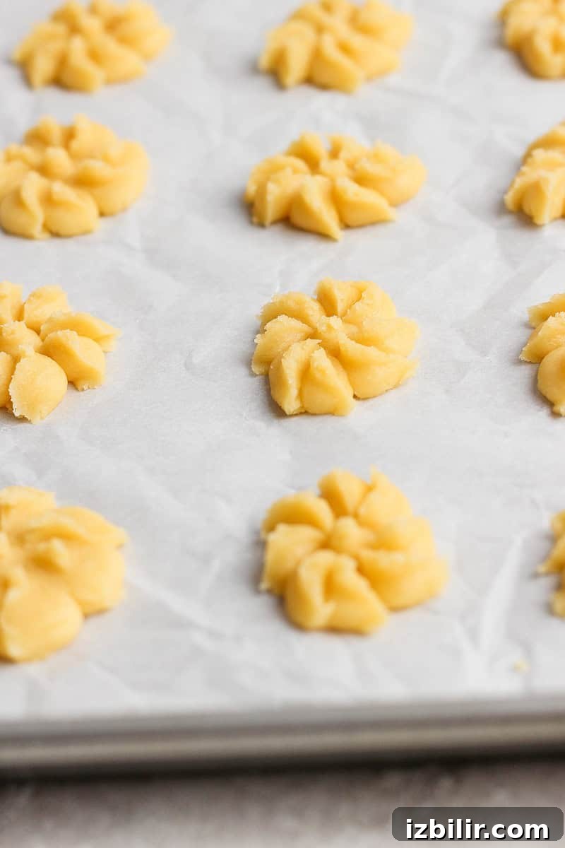 Raw cookie dough shaped into floral patterns on a parchment-lined baking sheet.
